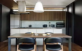 木目調のキッチンとダイニングテーブルが並ぶ、洗練されたモダンなインテリア。黒の椅子と白い照明が空間を引き締める。