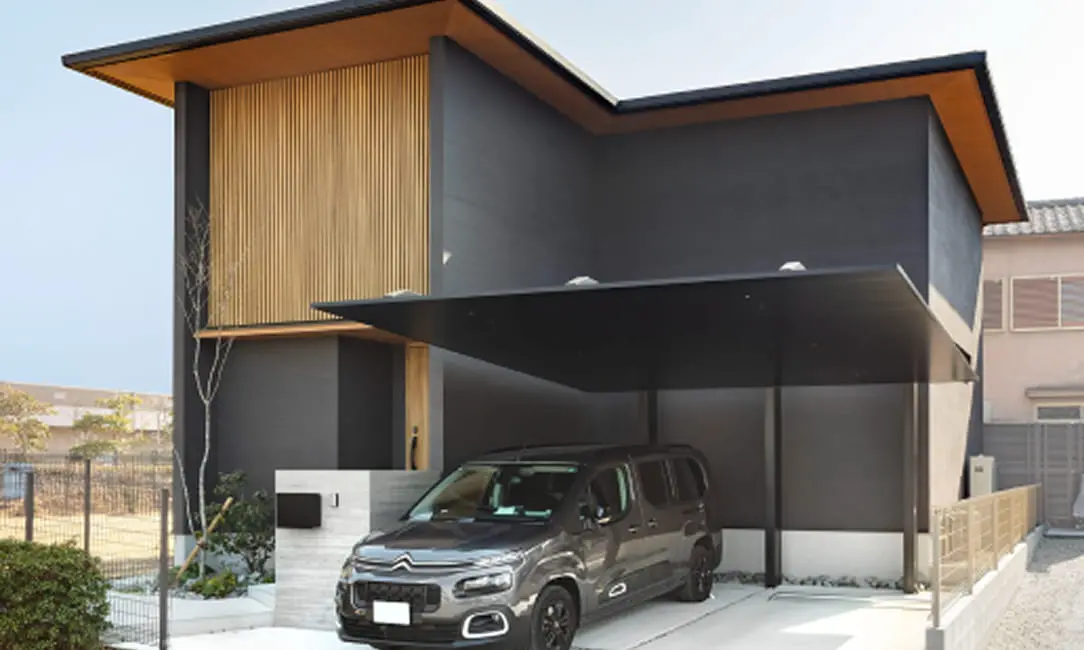 黒い外壁と木のアクセントが印象的な二階建て住宅。スタイリッシュなカーポートに車が停められている