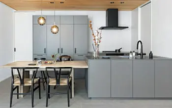 グレーで統一されたアイランドキッチンと収納、木のダイニングテーブルが並ぶ洗練された室内。天井は木目、床はグレーのタイル張り。