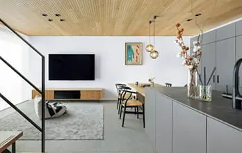 木目天井とグレートーンで統一された、洗練されたLDK空間。壁掛けテレビ、北欧風ダイニングセット、アイランドキッチンが並び、上品で温かみのある雰囲気。