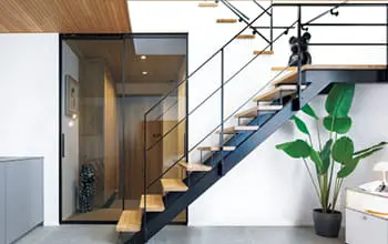 木製ルーバーと白壁が調和したモダンな二階建て住宅。軒の深い屋根と豊かな植栽が特徴で、落ち着いた佇まい。